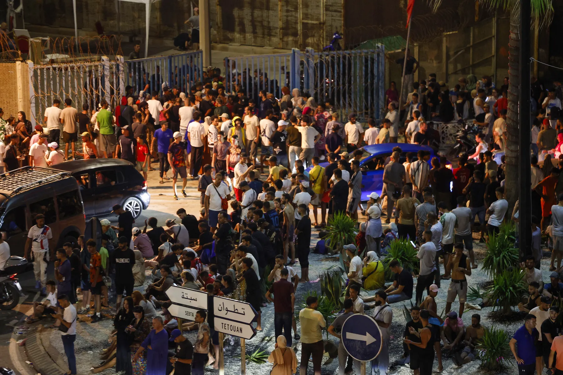 Cientos de personas concentradas de noche junto al paso fronterizo, con carteles que señalan a Sebta y Tetuán