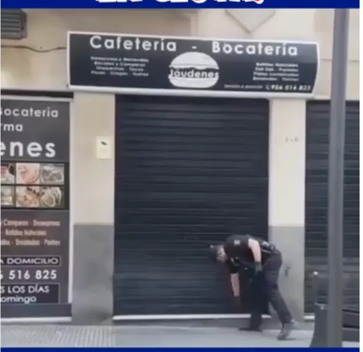 Fotograma del vídeo: un agente de Policía Nacional agachado frente a la persiana bajada de una cafetería en Ceuta